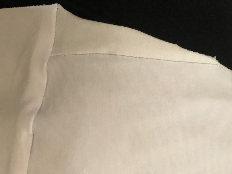 Closeup of the sewn on triangular section of the fabric with a black background. The trianlge is a right angle with the long end, at the bottom, attached to the front bodice to extend the panel. The left side is attached to the back bodice while the hypotenuse is along the sleeve part. 