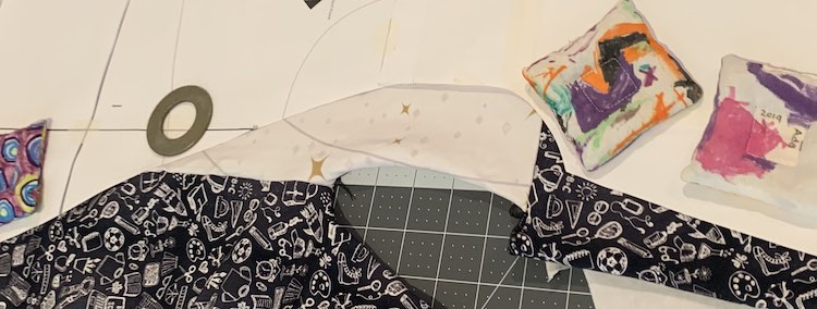 Image shows a part of the paper pattern with the fabric, both white and black, extending past the edge of the pattern. Underneath it all sits my cutting mat and above it all sits four of my pattern weights. 