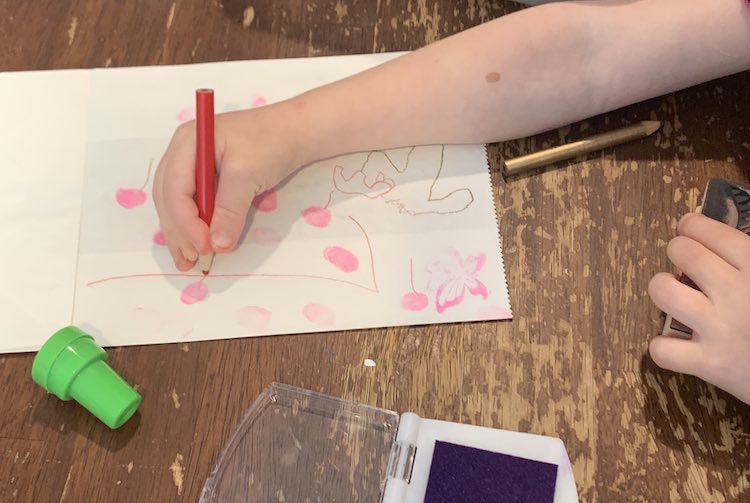 Over view of Zoey drawing a red line coming from one of the many pink fingerprints on the flattened paper bag in front of her. 