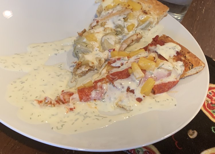 Closeup of a white plate with two different slices of pizza on top drizzled in ranch dressing. 