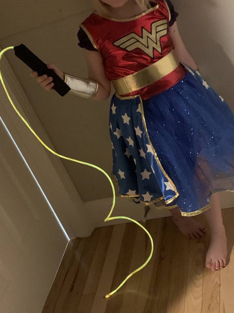 Wonder Woman holding up her lasso of truth. The black handle is in her hand and the glowing lasso hangs and drapes onto the floor. 