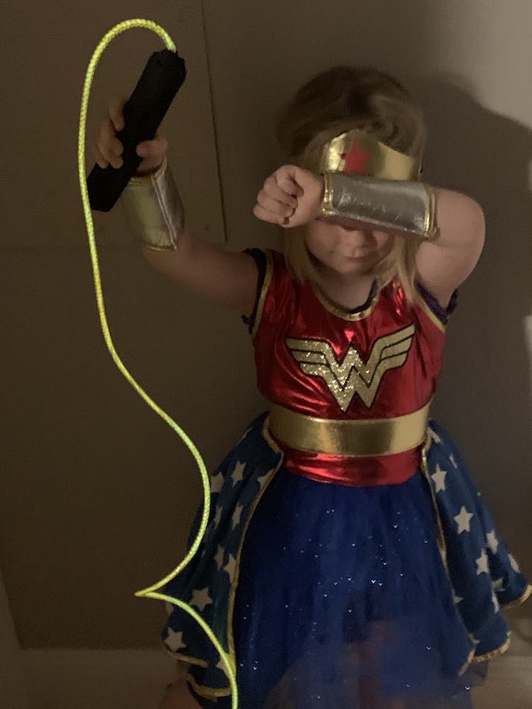 Image from above of Ada, as Wonder Woman, holding up the glowing lasso of truth, while blocking her face from attacks. 