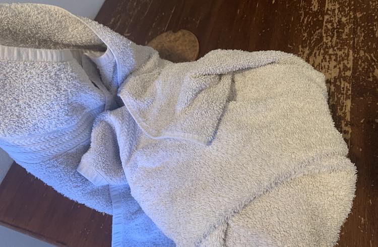 Image is taken above looking down at the towel wrapped up on three sides. The towel on the left side is held up still.