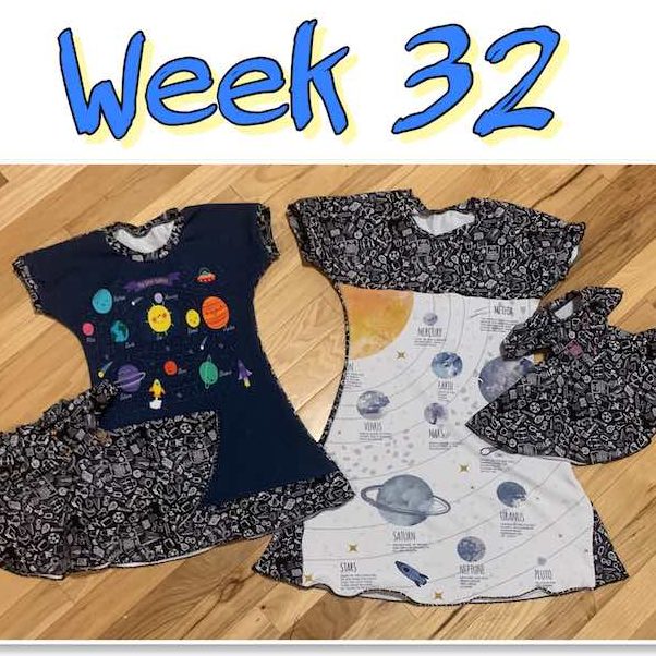 Image is a large title "Week 32" over a single framed photo showing two dresses side by side with small doll dresses overlapped. Teh larger dress has a white panel with planets and labels on it while the smaller one has a blue panel with cartoony planets and a sun. Both dresses are bordered in a black fabric with school-related doodles on it. The doll dresses use the school doodles fabric with the odd one colored in so they can be told apart.