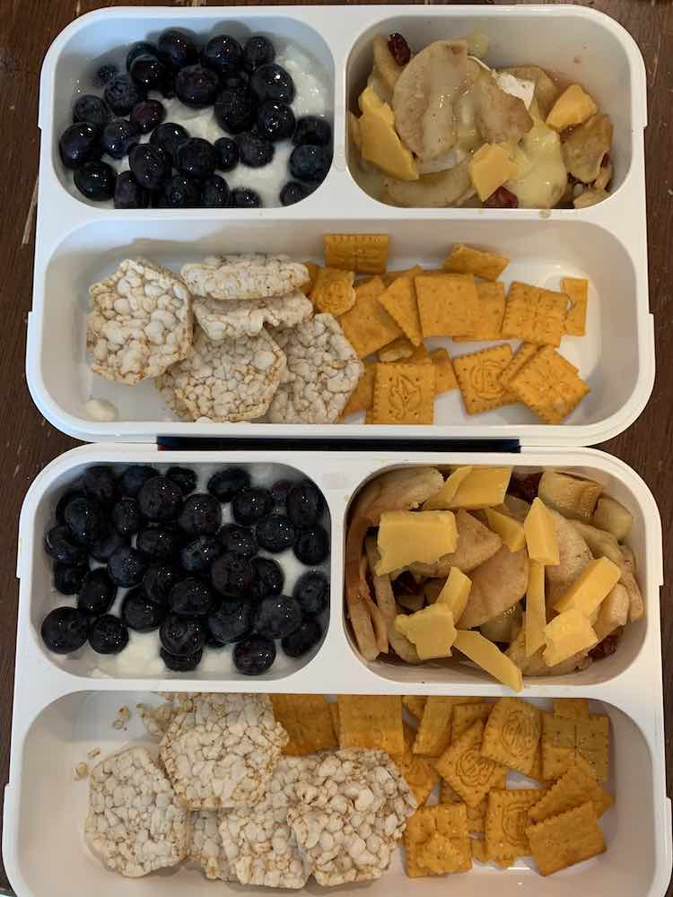Image is taken from above showing two lunch boxes, appearing to be above and below each other, with similar contents. The only difference is one lunchbox has melted brie apples while the other one has a more plain looking apple filling. 