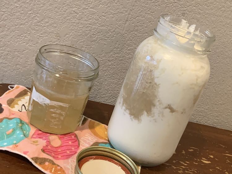 Image shows the lidless can of coconut simple syrup sitting on a flannel napkin on the table. Beside it sits a 32 ounce lidless glass canning jar mostly filled with white. In the center is the yellow-ish, in comparison, coconut.  