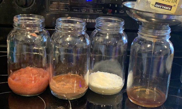 Image shows four clear canning jars sitting side-by-side on the stove. All have stuff in the bottom; from left to right the first has pink jam, the next has cocoa powder and honey, the third has white-ish liquid with white flakes on top, and finally the last one has honey, balanced upside down in a funnel above, drizzling down into a darkened pool from the vanilla extract.