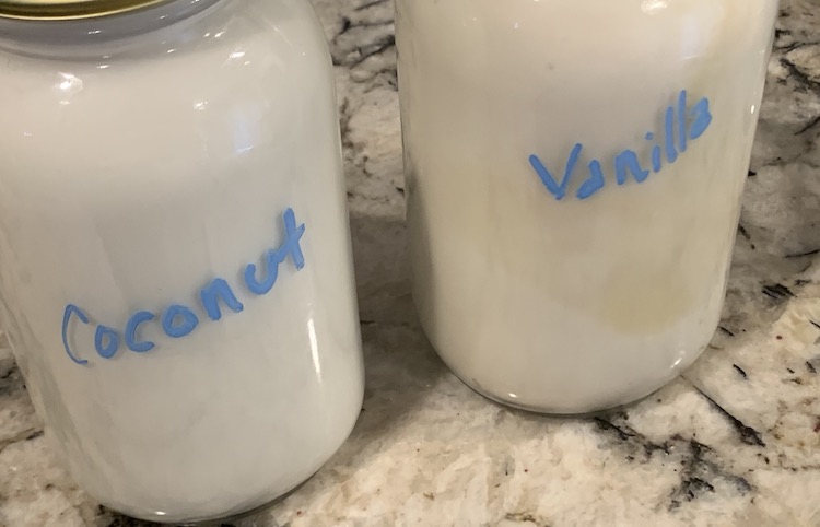 Closeup of two canning jars with blue letters. The one on the left is labelled coconut and is whiter than the slightly brown-hued jar on the right labelled vanilla. 