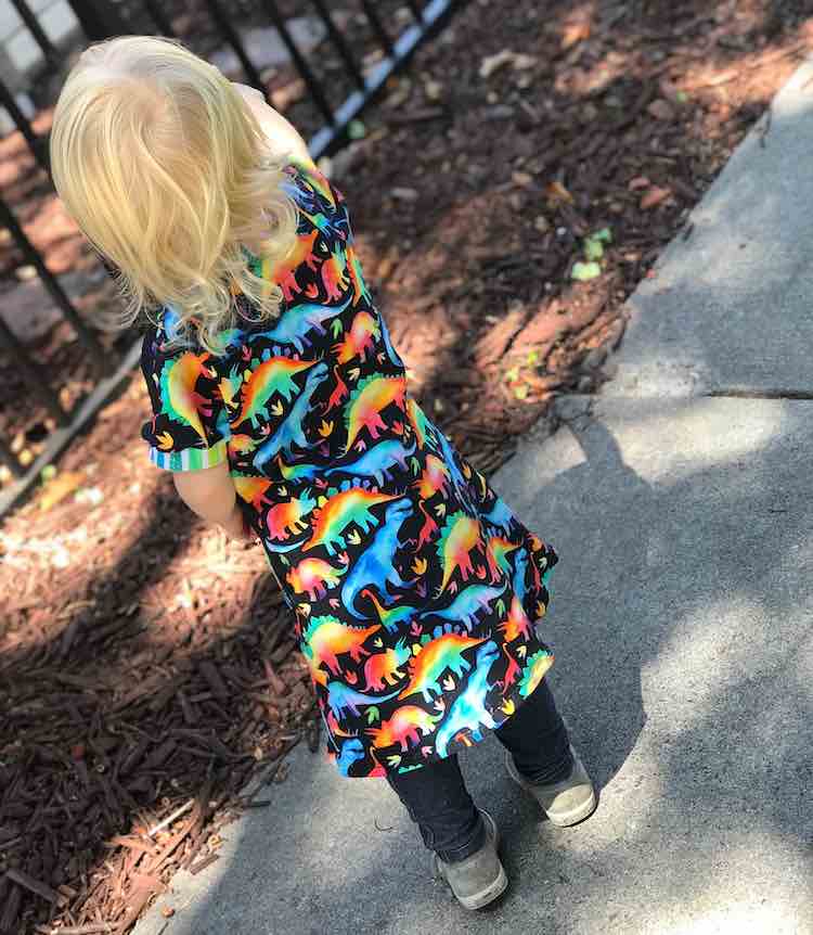 View of the back of Zoey's black dress with rainbow dinosaurs on it. You can see the back of the dress is all one piece with no seam so the dinosaurs aren't interrupted. 