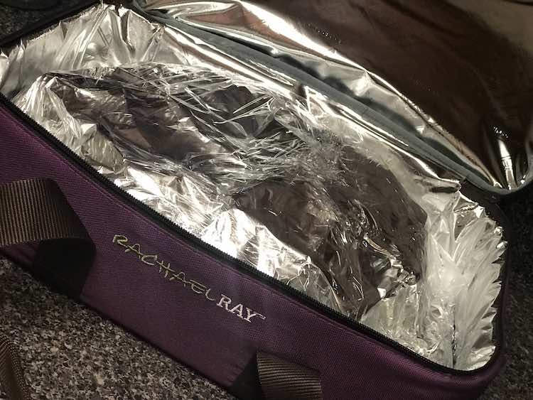 Image shows an opened purple insulated Rachael Ray casserole carrier. Inside the tinfoil wrapped bread blends in with the silver interior of the carrier.