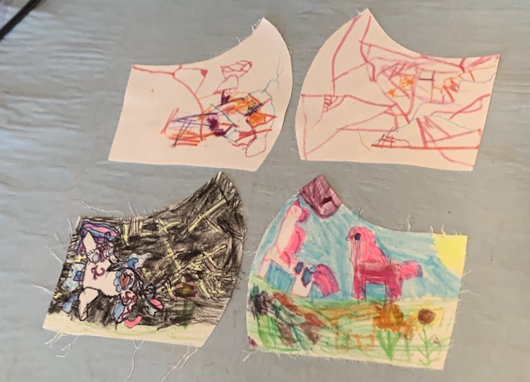 Image shows four, previously white, pattern pieces that had been colored by the girls. Zoey's two pieces are at the top and are more scribble doodled on while Ada drew a more detailed image to all the edges including unicorns, flowers, and the sun. 