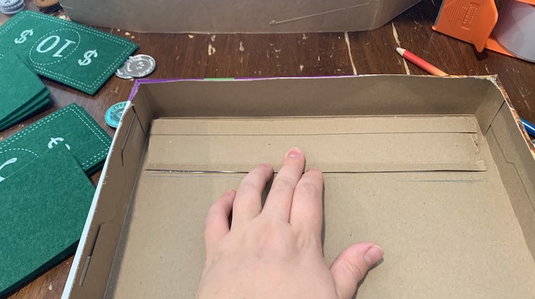 The strip from before is flipped over so it's along the top of the box and you can see the pencil marks below it and the tape showing through underneath it. My fingers are holding it down. 
