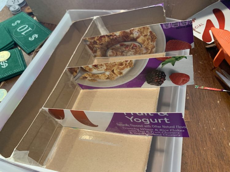 The cereal box organizer is tilted upwards in the plastic drawer as the three newly added dividers are too long to fit within the width of the drawer. 