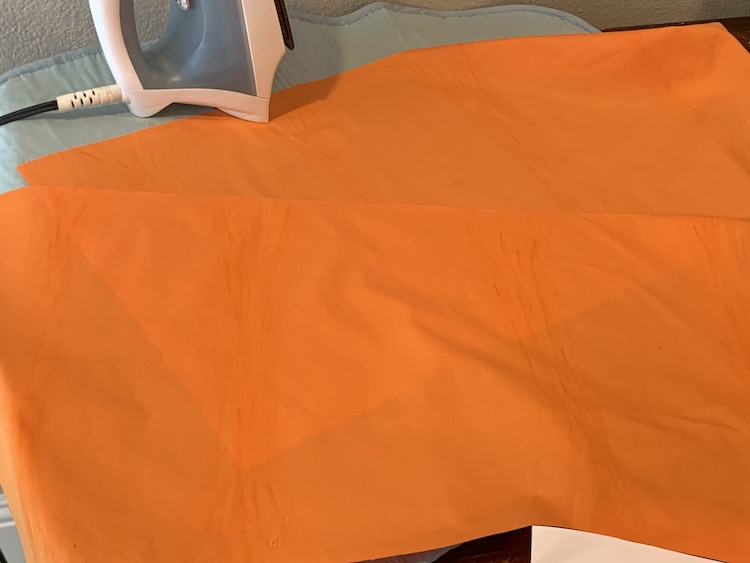 The two rectangles of orange fabric laid out on the ironing mat. 
