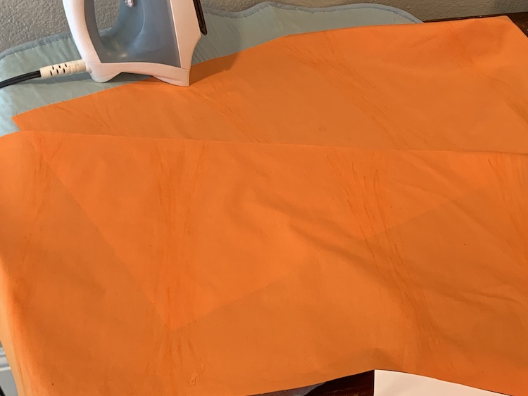 The two rectangles of orange fabric laid out on the ironing mat.