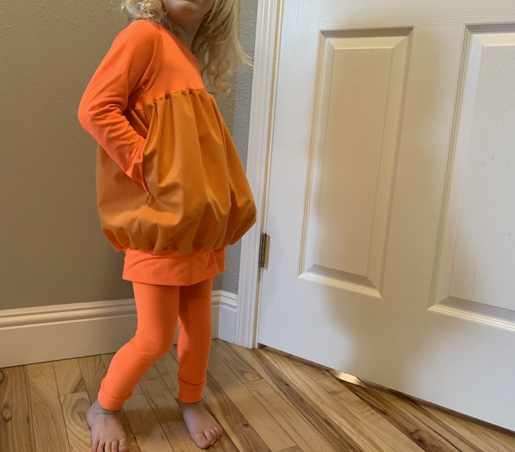 Zoey standing slightly turned with her hands in her pockets making the shirt look just a bit more pumpkin-esque.
