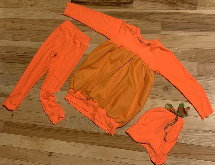 The image is taken from above showing a flat lay. The shirt is laid out in the center with the arms outstretched. Underneath the one arm are the leggings while the beanie is laid out under the other arm.