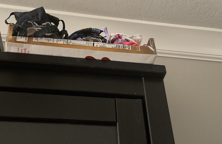 Image is taken from below looking up to towards the ceiling. It shows the top of the Ikea Billy cabinet with the organizer placed on top, slightly extending past the edge, with more masks stuffed inside compared to the image above.