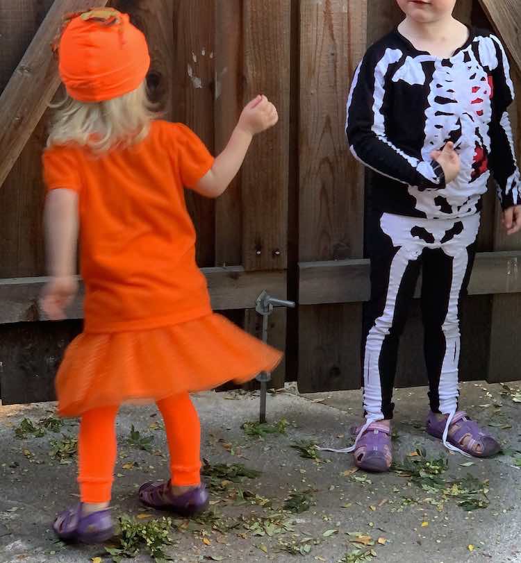 Image shows the back of Zoey's pumpkin costume as she twirls. To the right is Ada's swaying skeleton. 