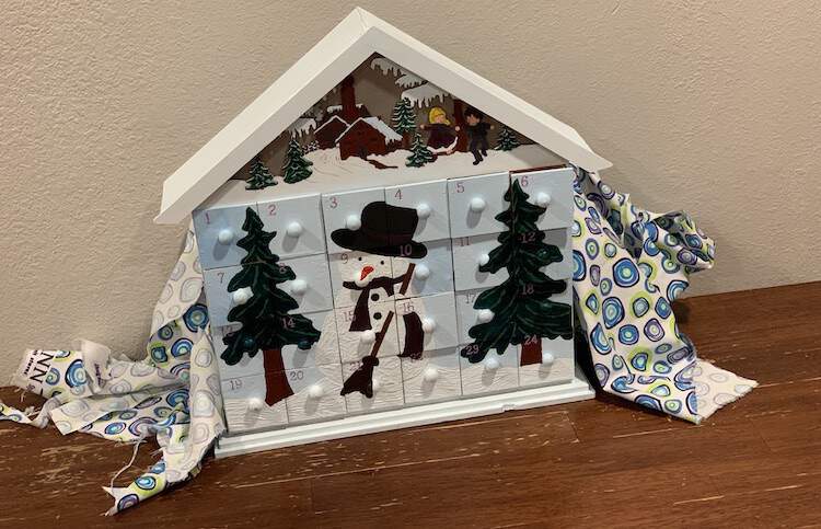 Image shows the advent calendar with all the drawers in place sitting on the table with white dotted fabric tossed behind it.