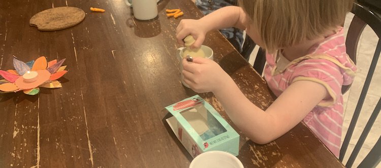 Image shows a kitchen table with a kindergarten Thanksgiving candle and a mug with a chocolate snowman being held inside it.
