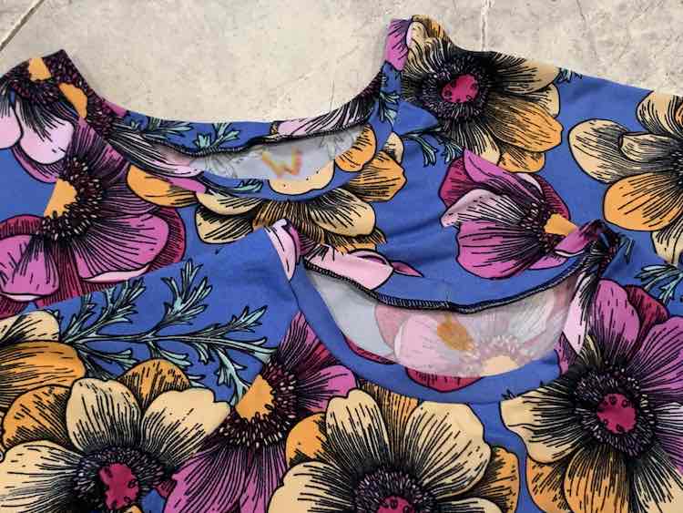 Image shows the top of two blue shirts with pink and orange flowers laid out over top of each other on the floor. Right under the neckband, on the inside back of the shirt, sits a "W" and a vague orange circle to help differentiate the two tops.