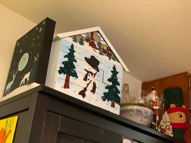 Image is taken looking up at the top of the cabinet showing two advent calendar, a berry strainer, and some Christmas decorations. 