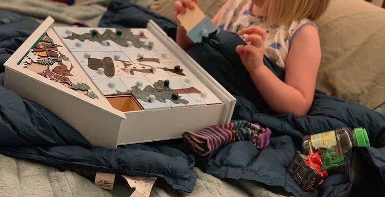 Ada sitting on the bed building hte advent calendar laid out on her lap with a sock, a car, and a container of plastic dinosaurs beside her. 