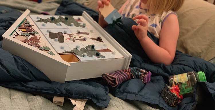 Ada sitting on the bed building hte advent calendar laid out on her lap with a sock, a car, and a container of plastic dinosaurs beside her.