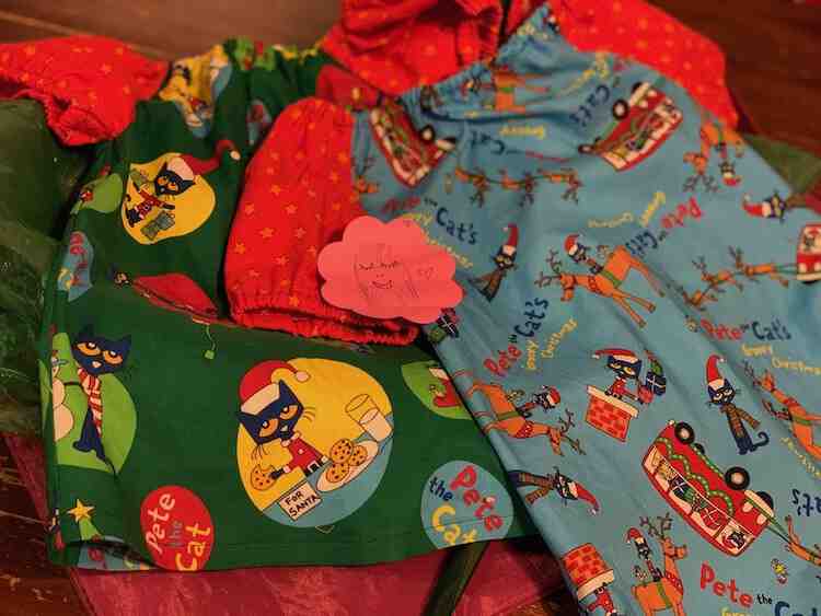 Image shows the two shirts laid out on the table on top of fabric gift bags. On the center sits a pink post-it note with a person's face drawn on with closed eyes.