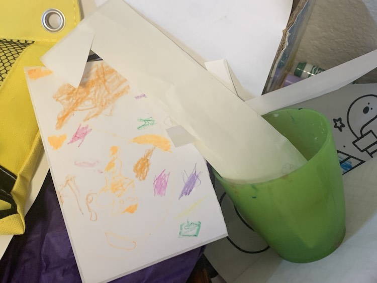 Image shows a cup with blank, and mine, stickers along with Zoey's designed sticker sheet sitting on top of a pile of papers and art supplies. 
