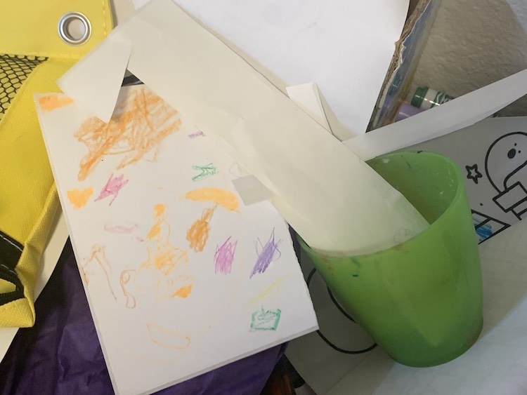 Image shows a cup with blank, and mine, stickers along with Zoey's designed sticker sheet sitting on top of a pile of papers and art supplies.