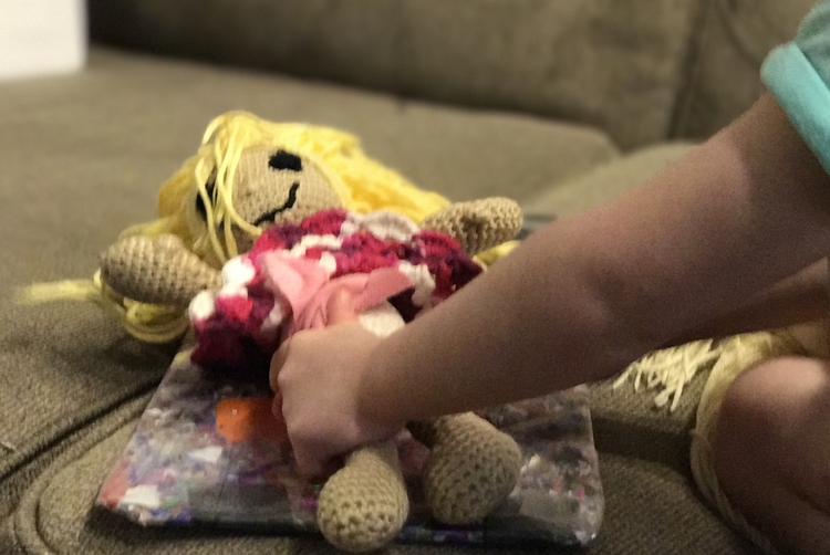 Ada reaches over and works on the diaper while the crocheted doll lays on changing pad.