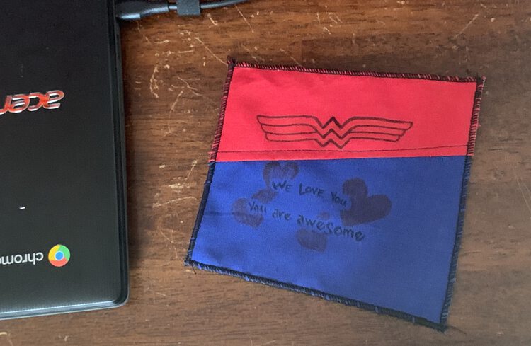 Image shows the finished black edged red and blue Wonder Woman coaster on a brown surface next to the laptop.