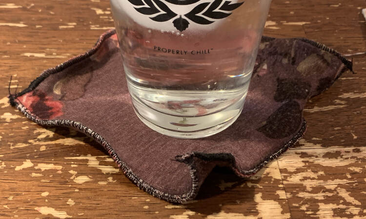 Image shows an icy glass of water sitting on a rippled black edged flowered coaster on the table. 