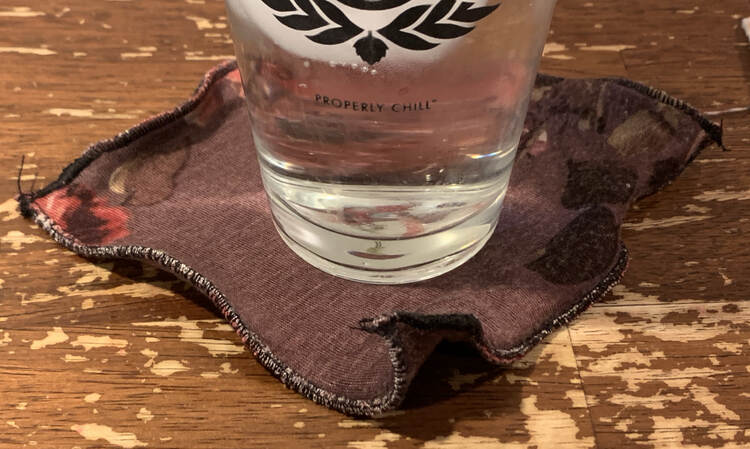 Image shows an icy glass of water sitting on a rippled black edged flowered coaster on the table.