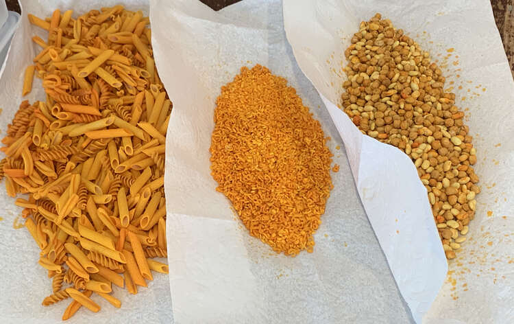Image shows three piles of yellow sensory material laid out on overlapping paper towel. From the left to right it's a mix of large pasta, rice with alphabet pasta, and two types of beans. 