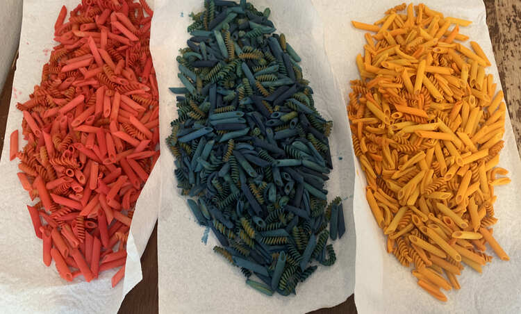 Image shows three sheets of paper towel laid overlapping side by side on the table. From left to right it's a pile of red, blue, and yellow mixed pasta. 