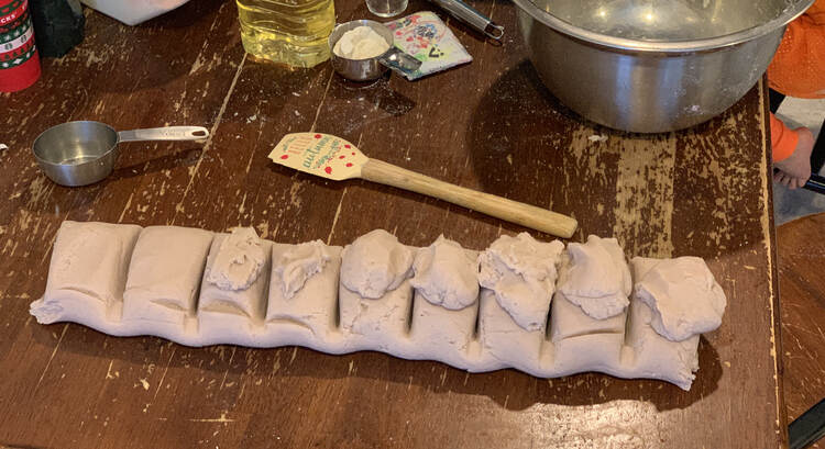 Photo shows nine equal-ish sections of playdough with my playdough-making tools laid out behind it. 
