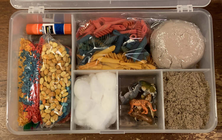 Image shows a sensory kit filled up with materials, glue stick, and toys. The lid is open to better see the contents. The items are listed in the caption below the image. 