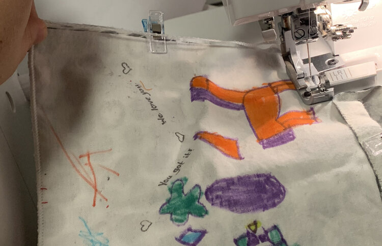 Image shows the coaster as the serger starts to serge the second side. You can see the excess fabric being trimmed away and the thread tail connecting the first side with the second side. 
