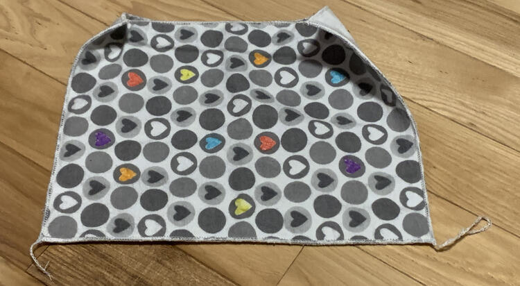 Image shows the backside of the finished coaster laid out horizontally. The hearts go sideways across it with the two bottom corners trailing a small thread tail. The top two corners and joined by a single shared tail so the corners are folded up towards each other.
