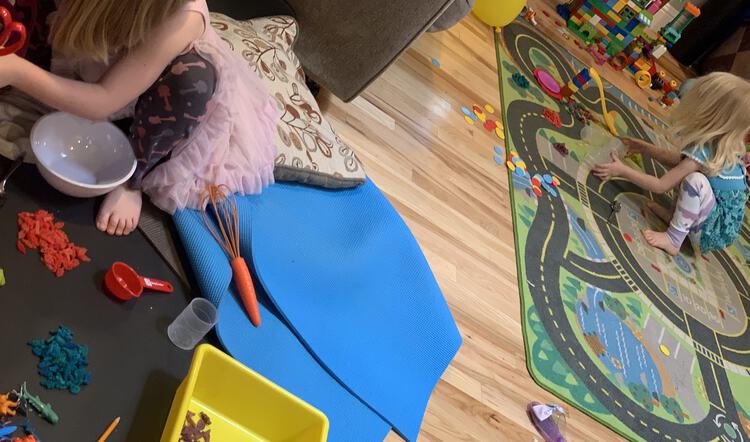 Photo shows the living room with Ada to the left making some food dish with her pasta dinosaurs. Zoey sits to the right with her dinosaurs waiting to go on the slide. 