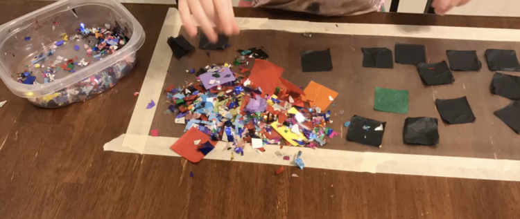 Image shows the same contact paper and container with supplies as the previous image. The difference is the pile of confetti and tissue squares dumped in the corner closest to the camera.