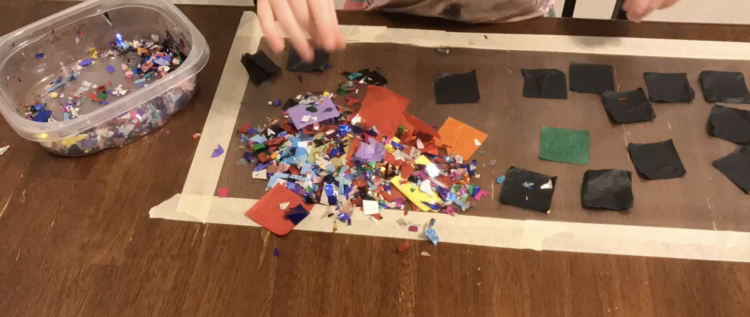 Image shows the same contact paper and container with supplies as the previous image. The difference is the pile of confetti and tissue squares dumped in the corner closest to the camera. 