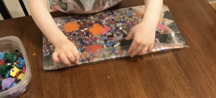 Image shows the decorated change pad laid out on the table. Ada is leaned over and folding over the excess con-tact paper closest to the camera.