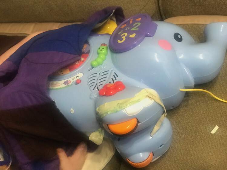Image shows a large plastic elephant pull toy being tucked under a blanket carefully with a masking tape bandage applied to it's foot.
