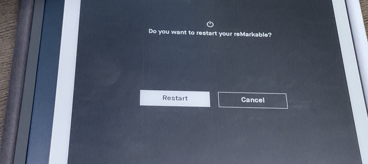 Image shows a closeup of the center of the reMarkable after the confirmation pops up. The message reads "Do you want to restart your reMarkable?" and there's two buttons below labeled Restart and Cancel. 