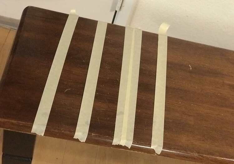 Image shows the end of the bench from above. On it is three strips of masking tape and one strip (second from the right) with two strips overlapping slightly. 
