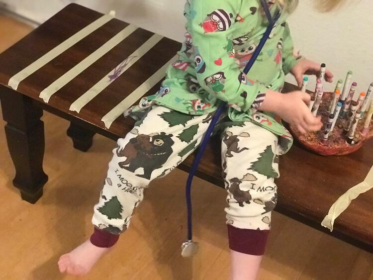 Image shows the bench with Ada sitting in the center reaching over for markers while a stethoscope hangs from her neck. There's tape stripes on either side of her on the bench. 